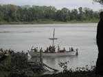 Photo:  The white pirogue arrives at the US Army’s Belle Fontaine Cantonment on the Missouri River, carrying members of the Corps of Discovery at the end of their expedition. 