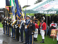 Photo: Members of the multi-Service color guard (U.S. Army, U.S. Air Force, U.S. Navy and U.S. Coast Guard) prepare to present the Service Flags, State Flags, and National Colors at the Fort Stevens opening ceremony.  Several members of the Lewis and Clark Fife and Drum Corps, dressed in Jeffersonian Army musicians' uniforms, can be seen immediately to the rear of the color guard.  The corps is one of America's few all-youth corps, with members ranging in age from 10 - 18.  The young musicians play replica fifes and rope-tension drums used during the Eighteenth and Nineteenth centuries.  Their uniforms are red wool coats and bearskin crested hats, patterned after those of U.S. Army field musicians of the period 1804 - 1810.