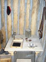 Photo: This probably represents a typical scene in First Sergeant Ordway’s quarters since the table holds a writing tablet, quills, and a lantern necessary for Ordway to dutifully make daily journal entries at night following completion of his daily duties. 