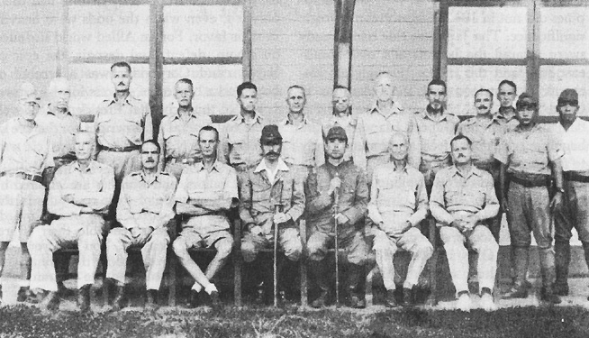 Photo:  American generals in captivity, July 1942.  Seated, left to right: Generals Moore, King, and Wainwright; two Japanese officers; Generals Parker and Jones. Standing, left to right: Japanese messenger; Generals Lough, Funk, Weaver, Brougher, Beebe, Bluemel, Drake, McBride, and Pierce; Colonel Hoffman (interpreter); and two Japanese soldiers.
