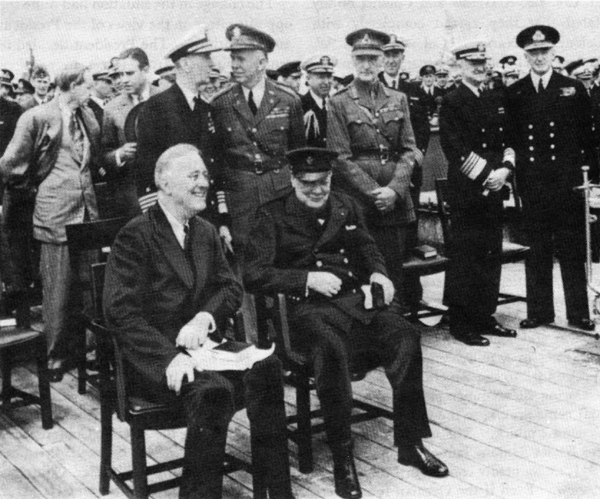 Photo - ABOARD THE H. M. S. PRINCE OF WALES during the Atlantic Conference. Seated: President Franklin D. Roosevelt and Prime Minister Winston S. Churchill. Standing, left to right: Harry Hopkins, W. Averell Harriman, Admiral Ernest J. King, General George C. Marshall, Field Marshal Sir John Dill, Admiral Harold R. Stark, and Admiral Sir Dudley Pound.