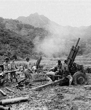 Men of the 122d Field Artillery Battalion, 33d Division, fire a 105-mm. howitzer against a Japanese pocket in the hills of Luzon.